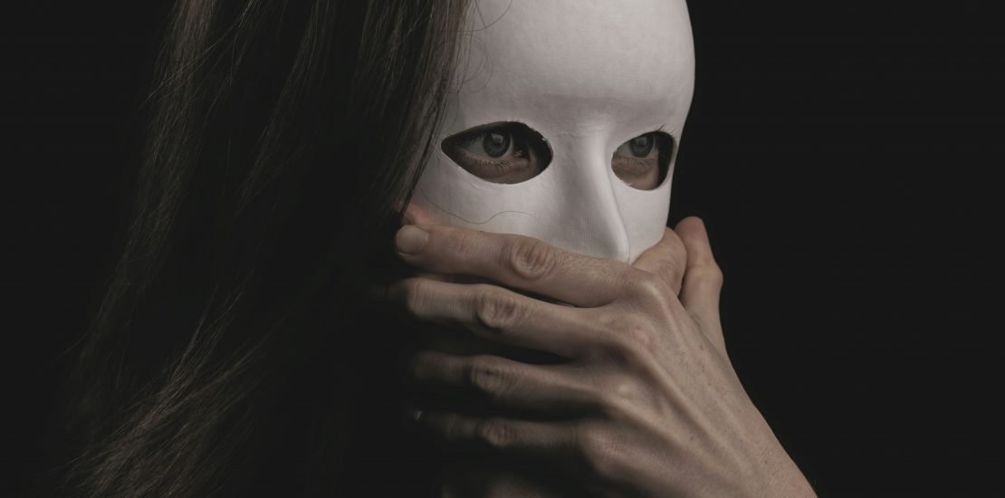 image of someone with long brown straight here wearing a white mask showing their eyes and their hand is covering the mask around the mouth.