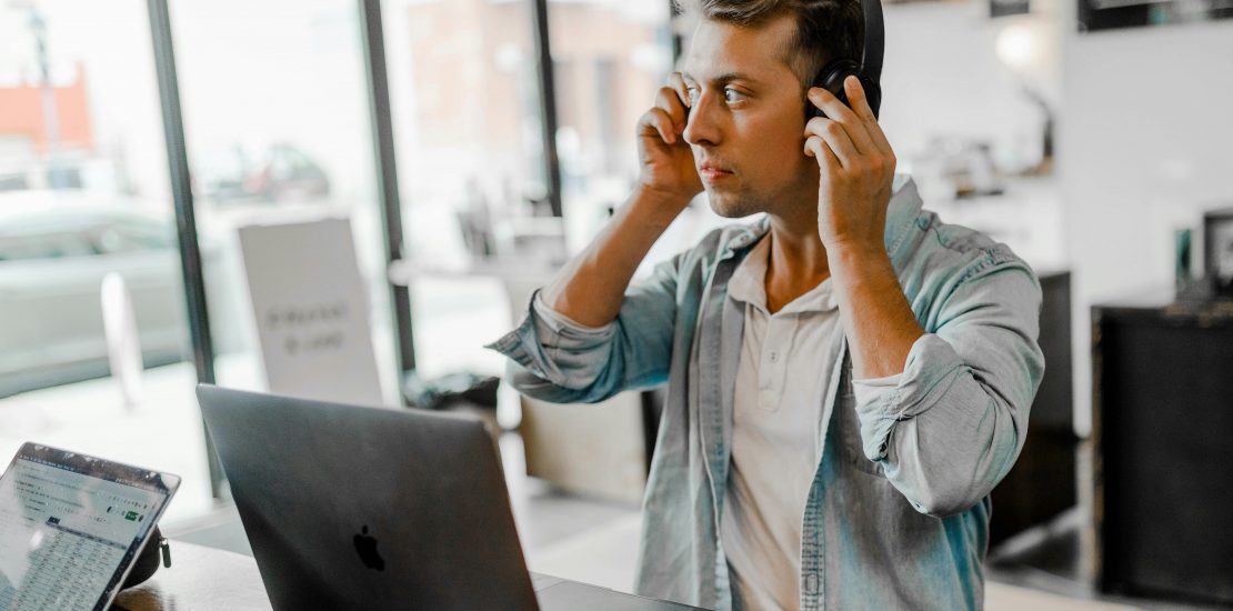 Man using headphones while working from a laptop in a bright office environment
