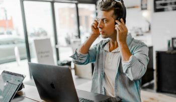 Man using headphones while working from a laptop in a bright office environment