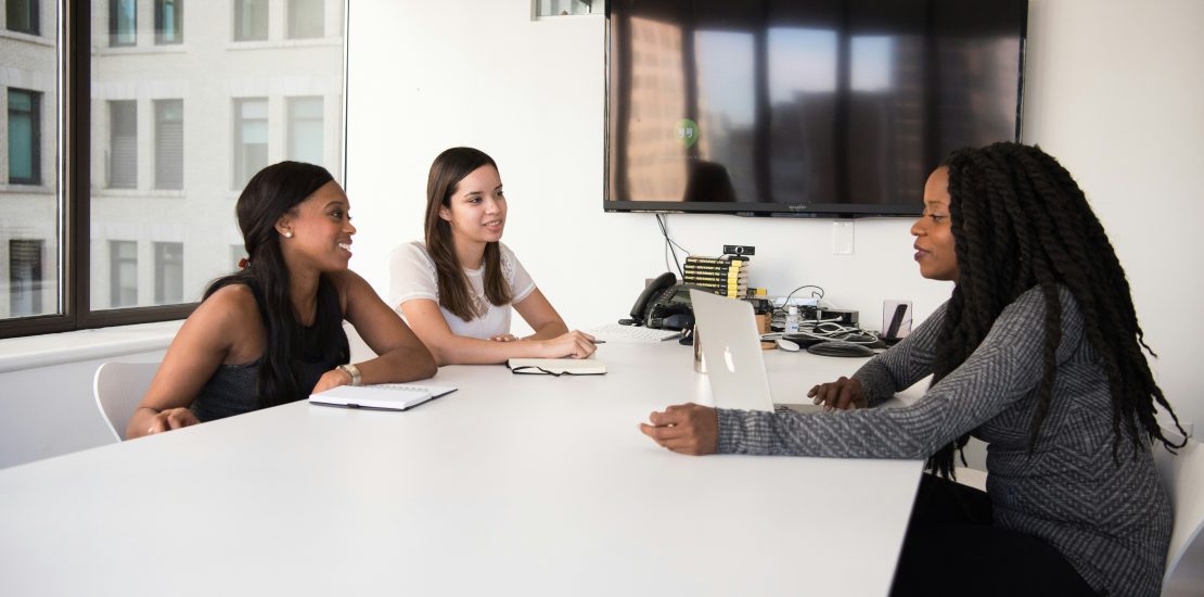 three women sat around an office table in an interview.