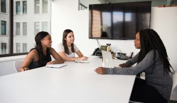 three women sat around an office table in an interview.