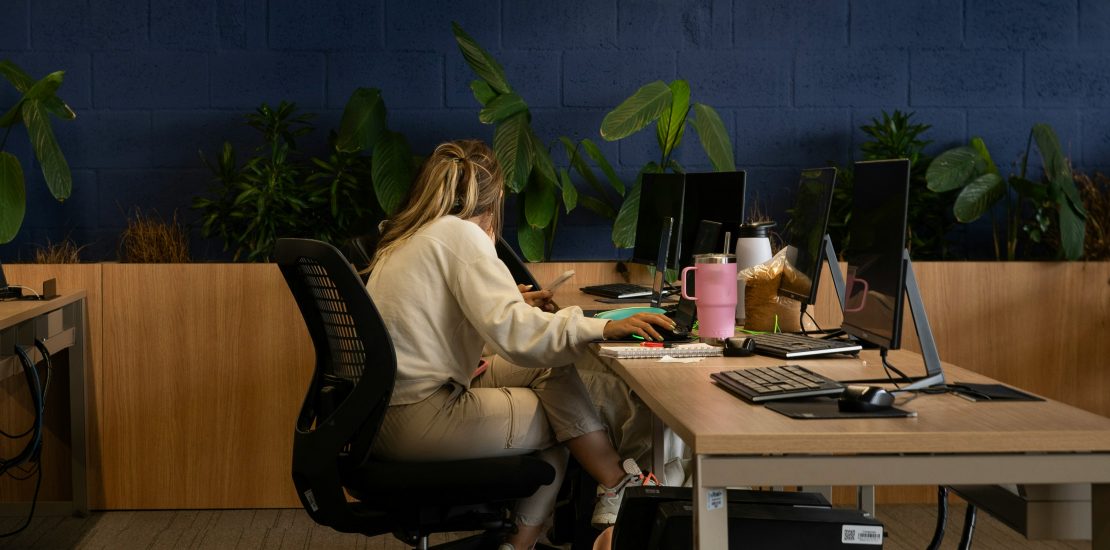 image of a woman sat in a row of desks in an office. She is by herself.