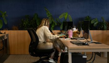 image of a woman sat in a row of desks in an office. She is by herself.